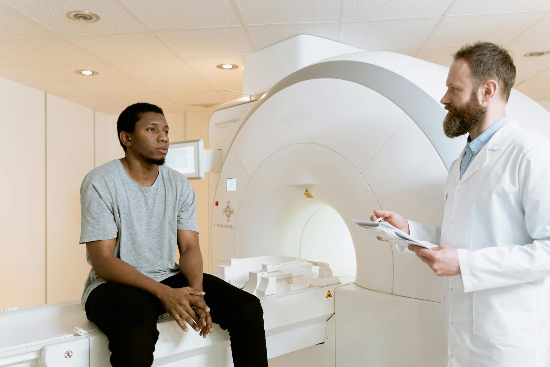 
                                    
                                        Doctor and patient discussing MRI results in a healthcare facility, with the patient sitting on the MRI scanner.
                                    
                                